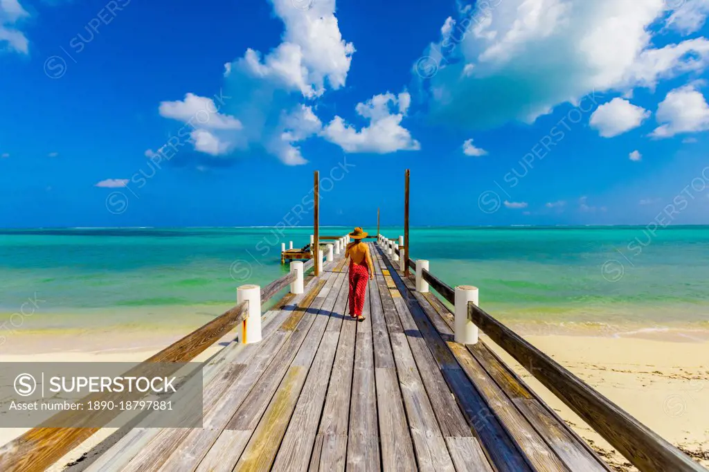Woman walking up the pier that stretches out into the ocean from Horse Stable Beach, North Caicos, Turks and Caicos Islands, Atlantic, Central America