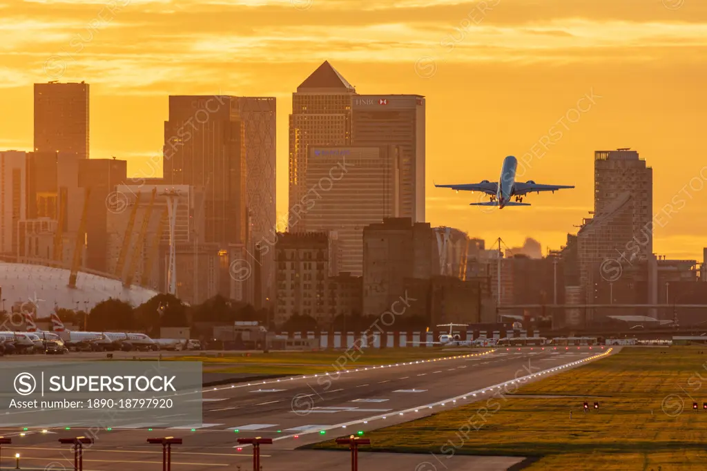 Aircraft taking off from London City Airport at sunset, with Canary Wharf and O2 Arena in background, London, England, United Kingdom, Europe