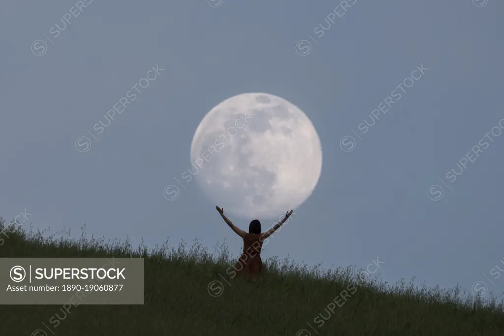 Full moon portrait at blue hour with a girl holding the moon above her head, Emilia Romagna, Italy