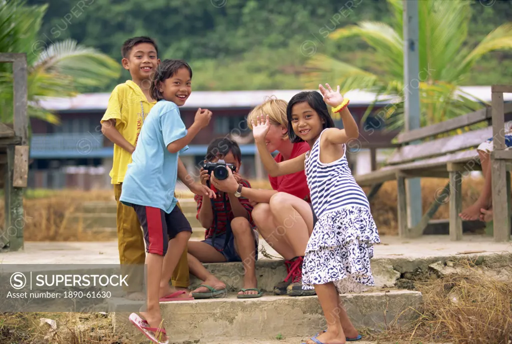 A group of Iban Dayak children with a tourist and camera outside their longhouse on the Rajang River near Kapit in Sarawak, northwest Borneo, Malaysia...