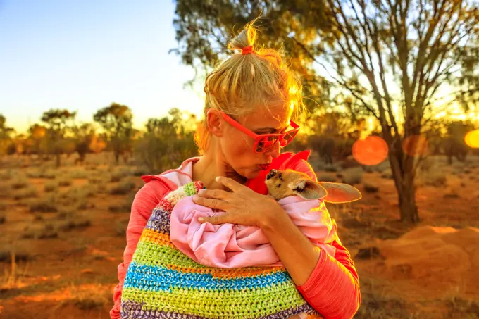 Tourist woman holding and kissing kangaroo joey at sunset light in Australian Outback, Red Center, Northern Territory, Australia, Pacific