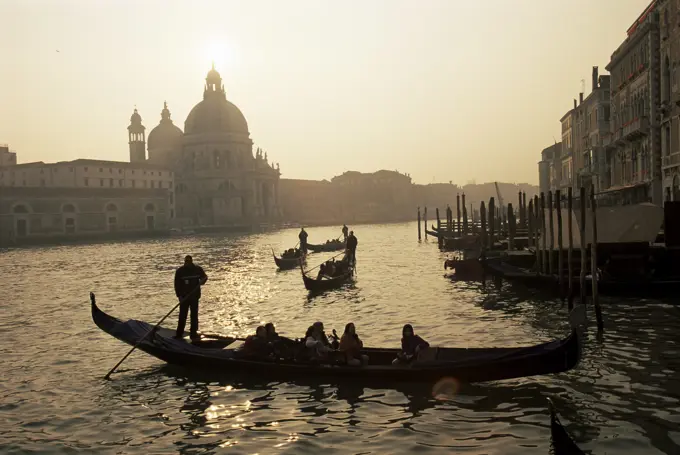 Sunset view along the Grand Canal to Santa Maria Della Salute church with gondoliers in silhouette, Venice, Veneto, Italy, Europe