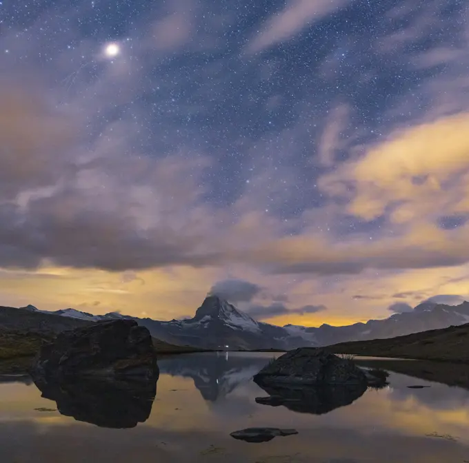 Matterhorn peak lit by moon in the starry night sky viewed from Stellisee, Zermatt, Valais canton, Switzerland, Europe