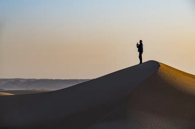 Man hiking through the sand dunes, Dirkou, Djado Plateau, Sahara, Niger, Africa