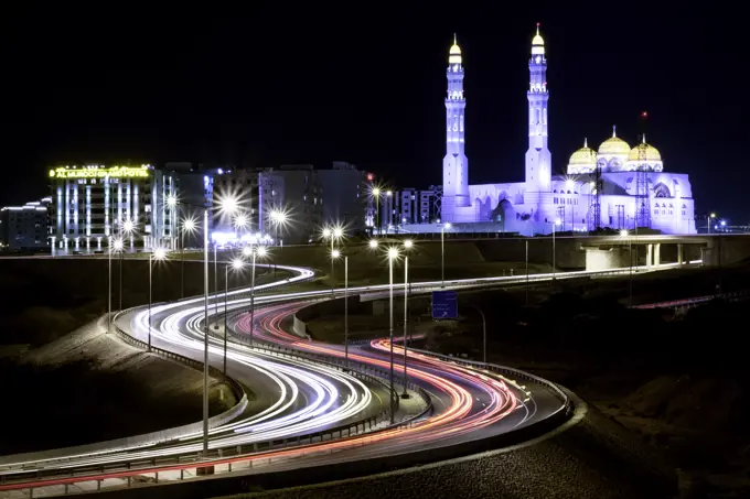 Long exposure cityscape night shot with a blue mosque and a street with car trails, Muscat, Oman, Middle East