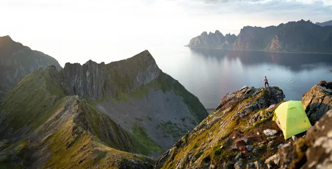 Tourist admiring sunset over the fjord out of camping tent, Senja island, Troms county, Norway, Scandinavia, Europe