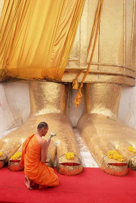 Buddhist monk kneeling in prayer at the feet of a statue of the standing Buddha, Wat Intharawihan, Bangkok, Thailand, Southeast Asia, Asia