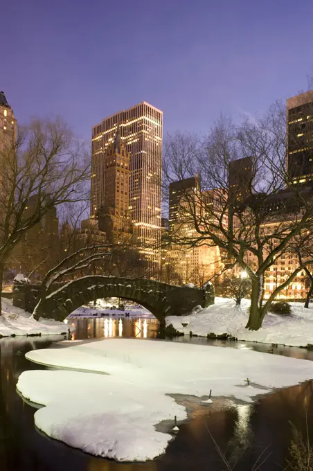 A view of the Gapstow Bridge in Central Park and city skyline at dusk after a snow storm, New York City, New York State, USA