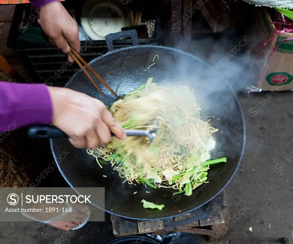 Woman cooking noodles in a street market, Myanmar