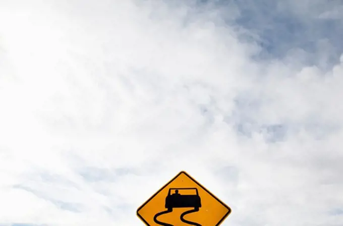 Slippery Road sign against a clouded sky