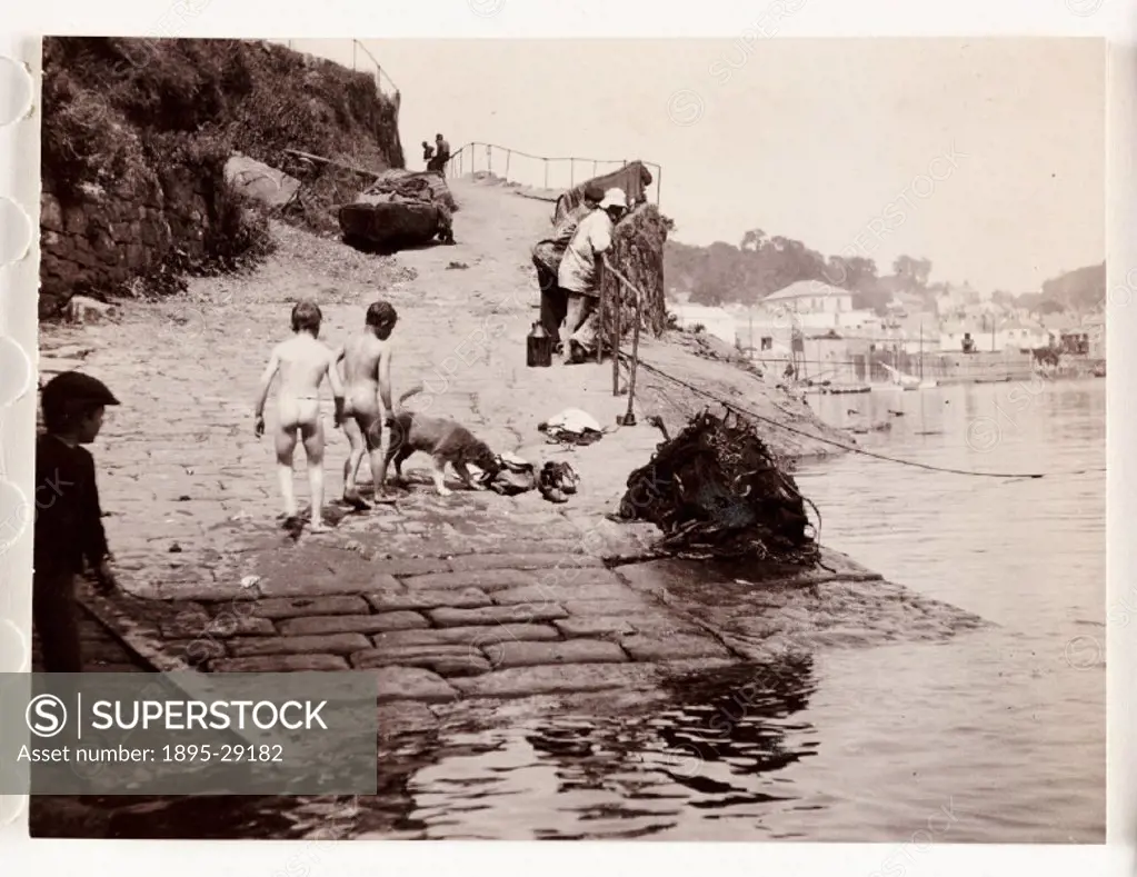 Photograph by Frank Meadow Sutcliffe (1853-1941) of naked boys walking up  the slipway out of the sea to dress after having a swim. Their dog sniffs  th... - SuperStock