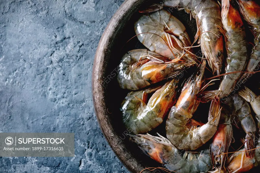 Raw uncooked prawns shrimp in clay plate. Dark concrete background. Flat lay. copy space