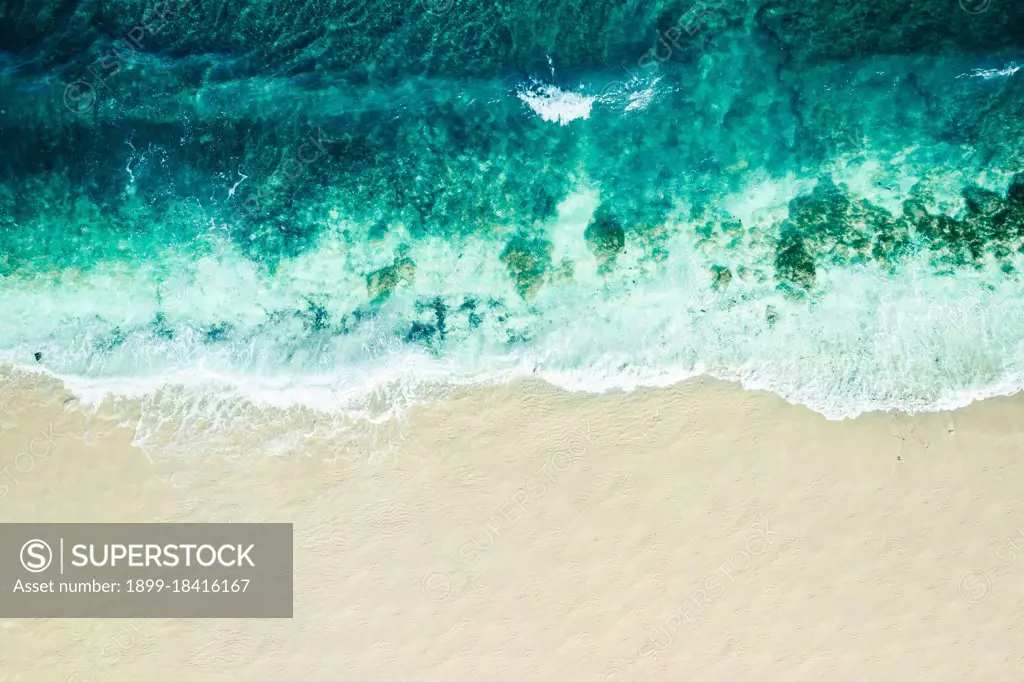 Aerial view looking down onto a tranquil cove with large waves breaking onto the beach