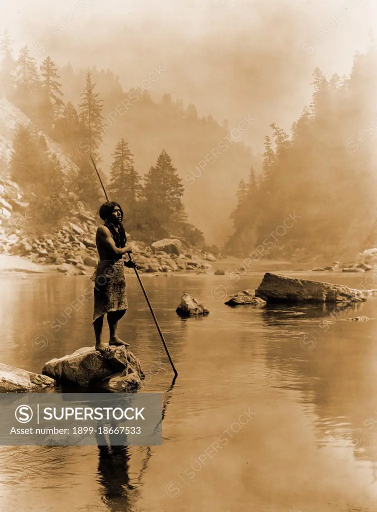 Edward S. Curtis Native American Indians - Hupa man with spear, standing on rock midstream circa 1923.