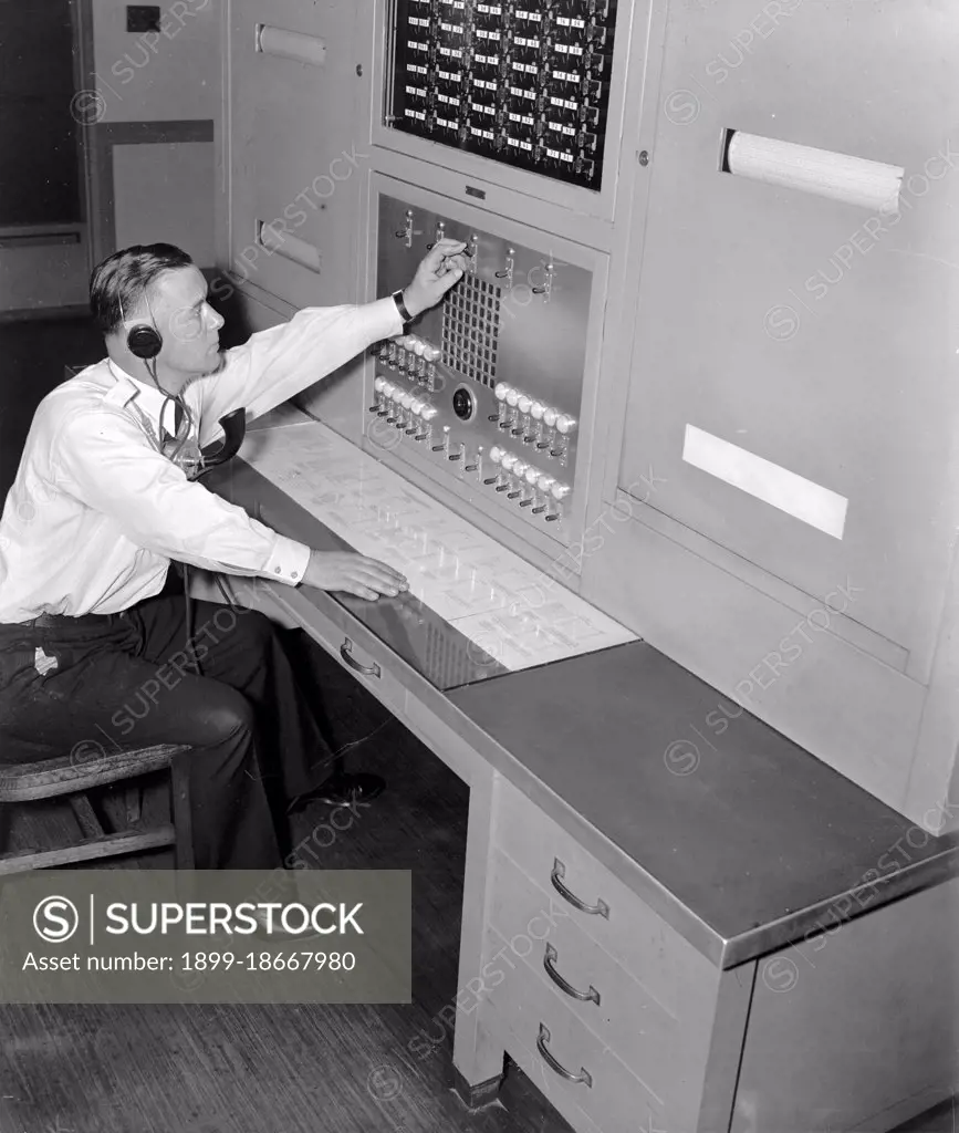 Officer William L. Good is shown at the FBI 'Patrol Board' in the Captain of the Guard's office which maintains direct communication with every watch station and substation throughout the huge FBI Headquarters building circa 1937.