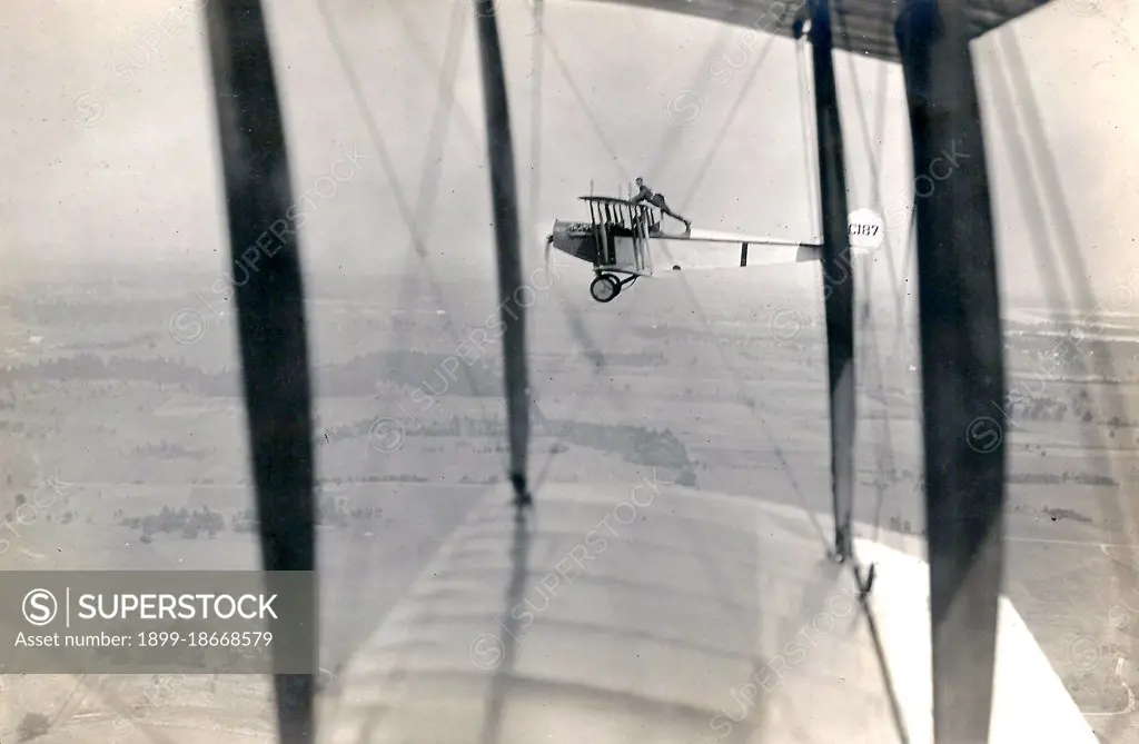 Photograph of Curtiss JN-4 aircraft C187 in flight, with a man Lieutenant Ned Ballough 'wing walking': standing with his arms on the top of the wing and his feet behind the back of the cockpit circa 1917.