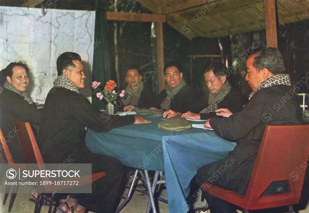 Wearing black peasant garb, chequed krama and with their Chinese military caps resting on the table, from the left closest to the map are Ieng Sary and then Hou Yuon. On the other side of the table, from the left are Pol Pot, Hou Nim and Khieu Samphan. At the end of the table sits Sihanouk.