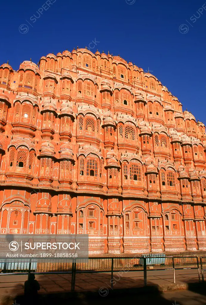 The Hawa Mahal was built in 1799 by Maharaja Sawai Pratap Singh, and designed by Lal Chand Ustad in the form of the crown of Krishna, the Hindu god. Jaipur is the capital and largest city of the Indian state of Rajasthan. It was founded on 18 November 1727 by Maharaja Sawai Jai Singh II, the ruler of Amber, after whom the city was named. The city today has a population of 3.1 million. Jaipur is known as the Pink City of India. The city is remarkable among pre-modern Indian cities for the width and regularity of its streets which are laid out into six sectors separated by broad streets 34 m (111 ft) wide. The urban quarters are further divided by networks of gridded streets. Five quarters wrap around the east, south, and west sides of a central palace quarter, with a sixth quarter immediately to the east. The Palace quarter encloses the sprawling Hawa Mahal palace complex, formal gardens, and a small lake. Nahargarh Fort, which was the residence of the King Sawai Jai Singh II, crowns th