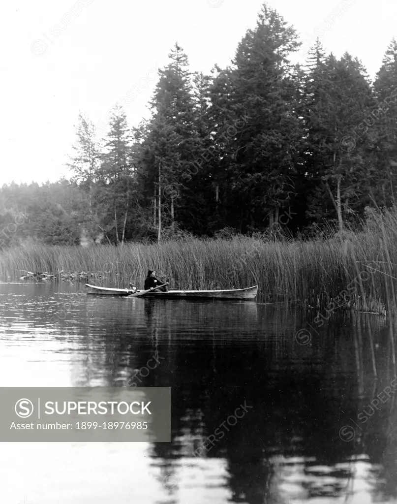 Edward S. Curtis Native American Indians - Quamichan woman paddles canoe near rushes at river's edge ca. 1910. 