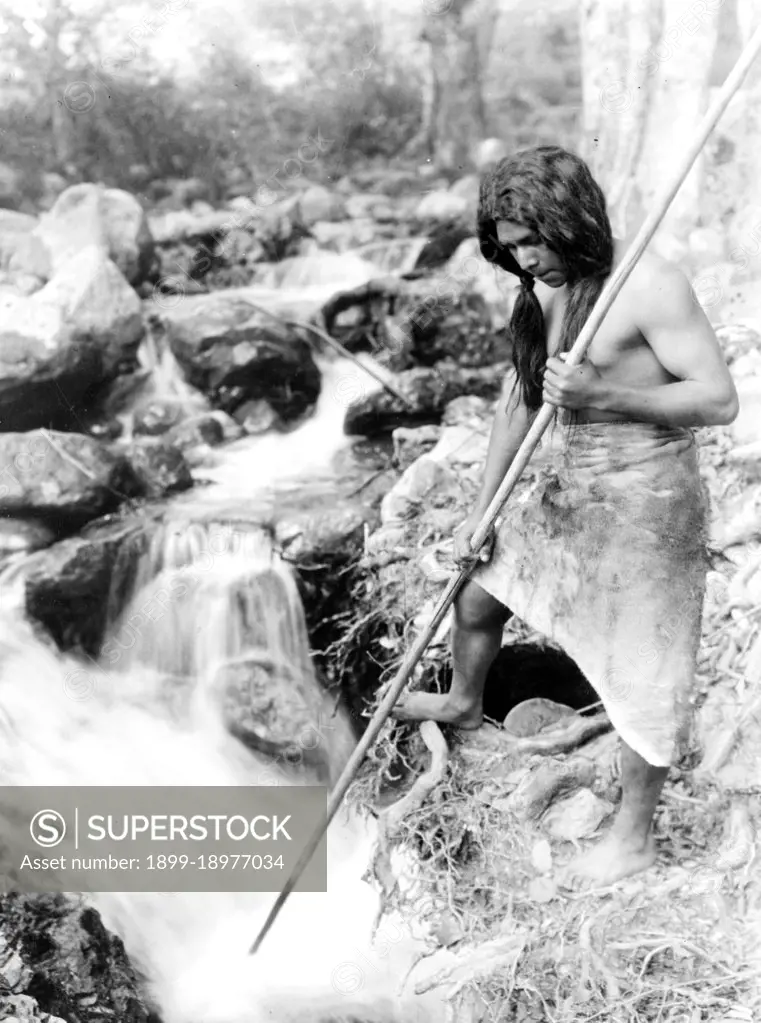 Edward S. Curtis Native American Indians - Hupa man with spear, standing on bank gazing into stream waiting for Salmon ca. 1923. 