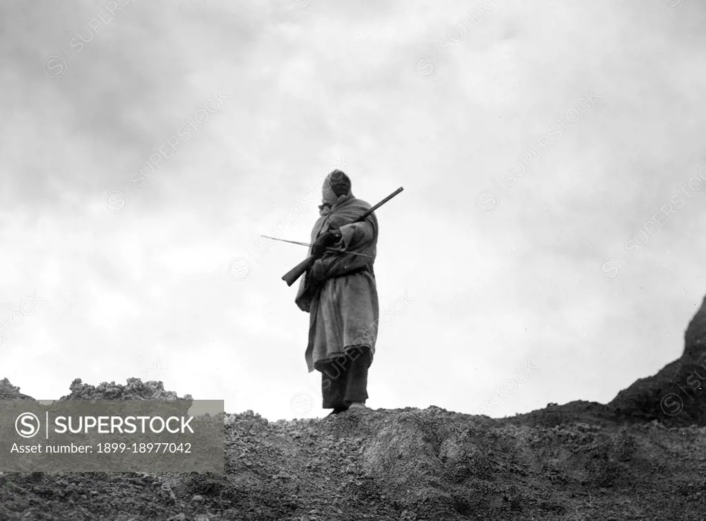 Sioux Indian standing holding a rifle and a bow. 