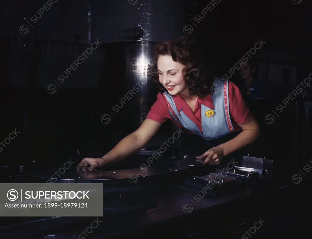 Metal parts are placed on masonite by this woman employee before they slide under the multi-ton hydropress, North American Aviation, Inc., Inglewood, Calif. - October 1942. 