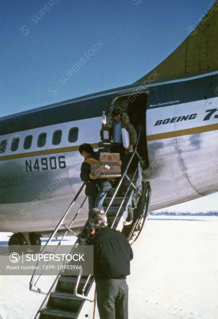 Carl Huntington and his wife exit a Wien Consolodiated airplane at Galena, Alaska, Carl is holding his trophy from winning the 1974 Iditarod Race ca. March 1974. 