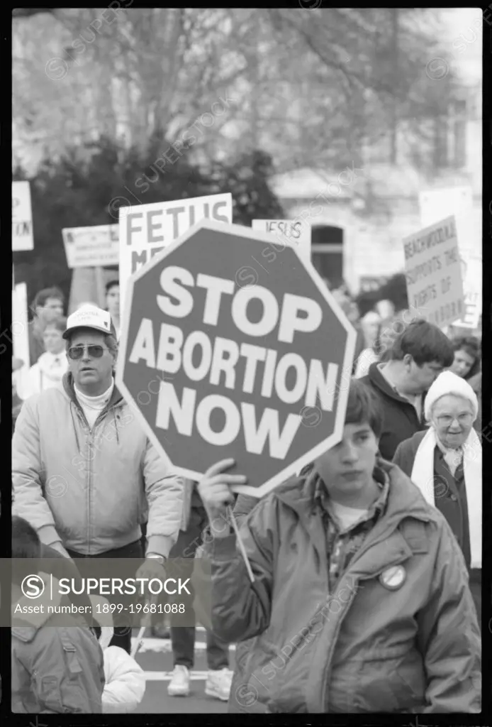 Young person holding a sign that has "Stop Abortion Now" written on it at a pro-life march, Washington, DC, 1/22/1990.