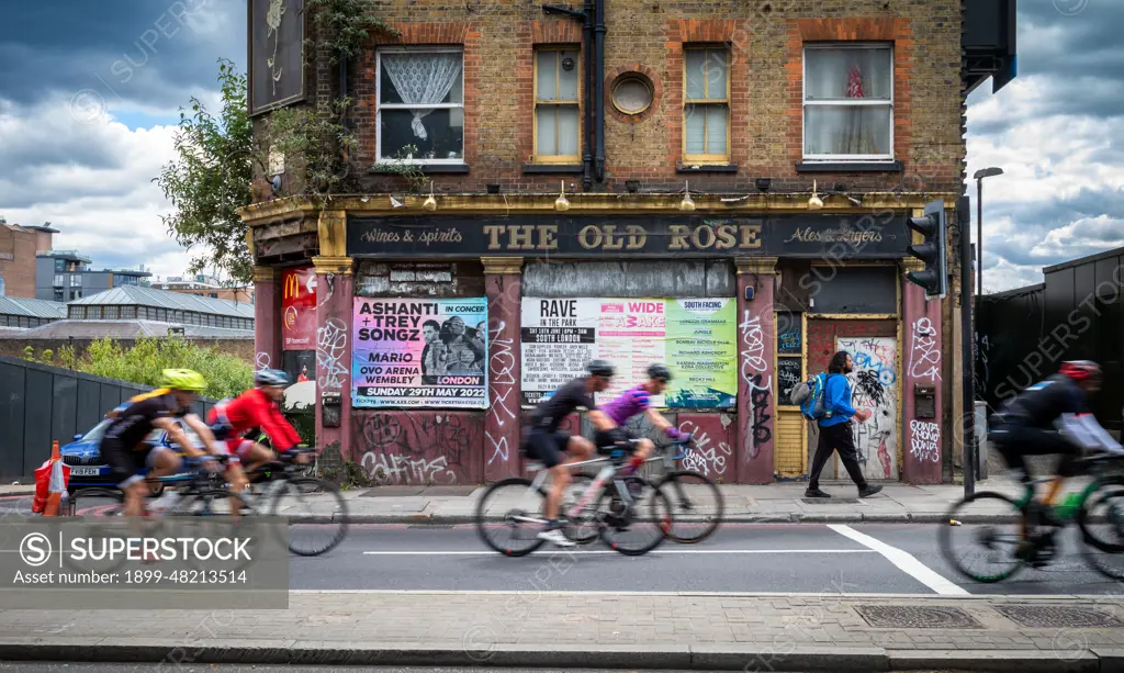 A group of cyclists participating in RideLondon 2022 pass a derelict pub called The Old Rose in the East End of London. The event was held for the first time since 2019 and the route took around 20,000 participants into Essex and across London.