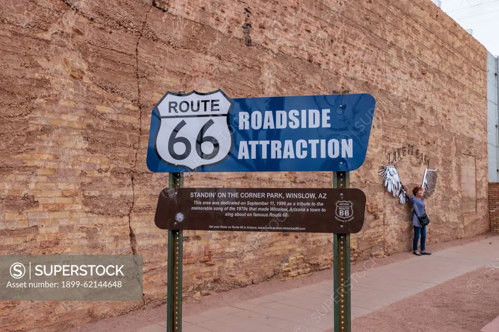 Woman posing for a photo behind roadside attraction sign at Standin' on the Corner Park in downtown Winslow, Arizona.