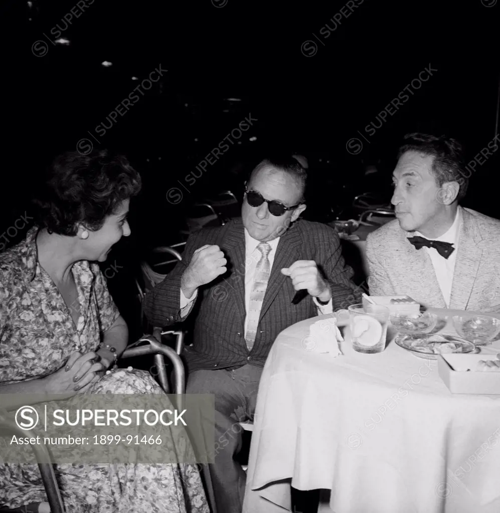 American journalist Victor Riesel talking to a man and a woman. The journalist is blind because of a stream of vitriol. Venice, August 1957