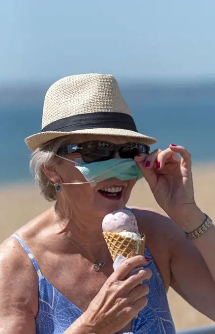 South sea, Portsmouth, Southern England, UK, Woman eating ice cream whilst wearing a mask and rubber protective gloves during the Corvid-19 outbreak On the beach in South sea