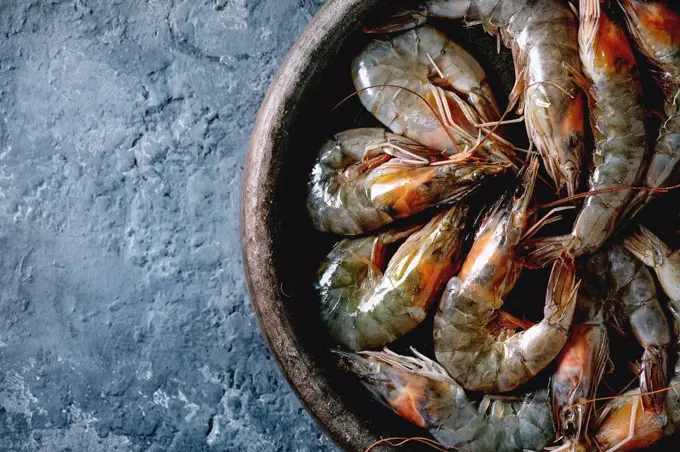 Raw uncooked prawns shrimp in clay plate. Dark concrete background. Flat lay. copy space