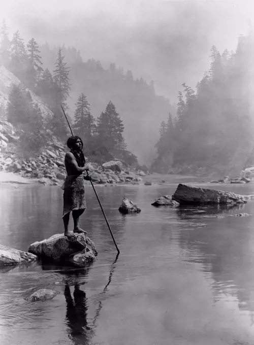 Edward S. Curtis Native American Indians - Hupa man with spear, standing on rock midstream circa 1923.