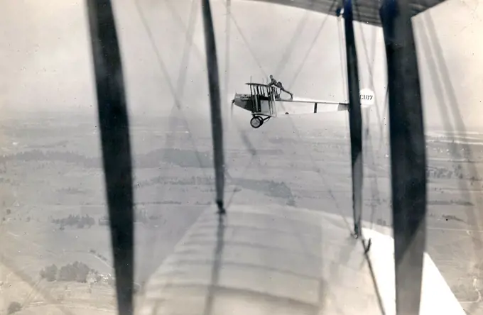 Photograph of Curtiss JN-4 aircraft C187 in flight, with a man Lieutenant Ned Ballough 'wing walking': standing with his arms on the top of the wing and his feet behind the back of the cockpit circa 1917.