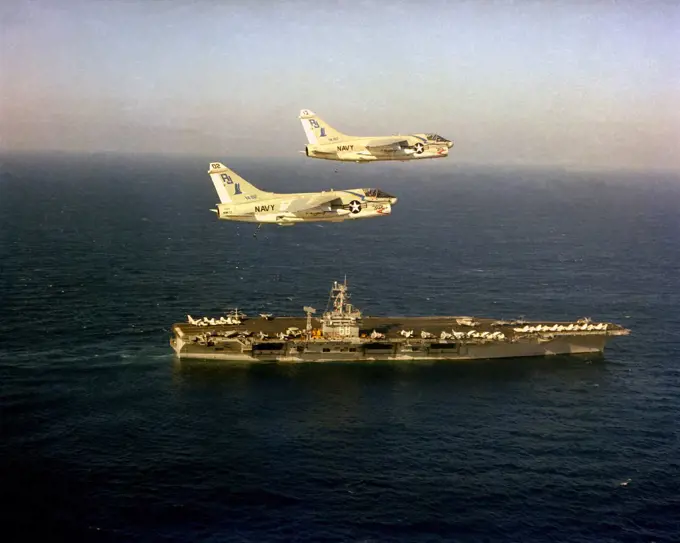 1979 - An aerial starboard view of the nuclear-powered aircraft carrier USS NIMITZ (CVN-68) underway with two A-7E Corsair II aircraft from Light Attack Squadron 82 (VA-82) in flight above the ship. 