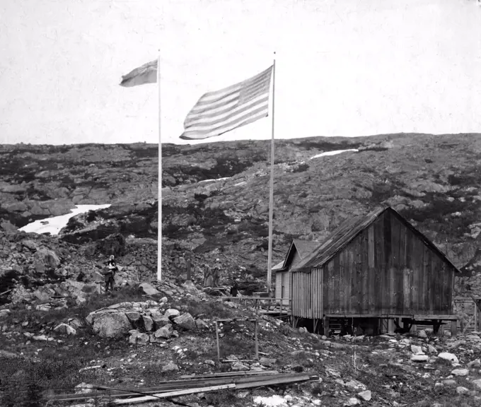 Alaska-Canada border with American and Canadian flags, a building, and people standing on either side. alaska yukon border 1900-23. 