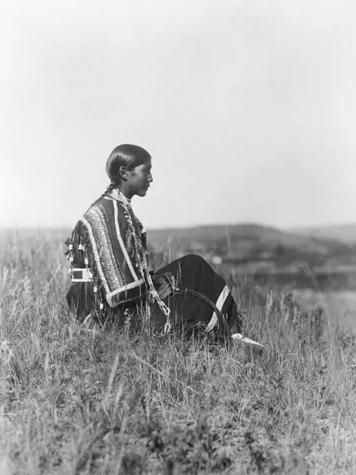 Edward S. Curtis Native American Indians - Young Piegan Indian woman, wearing beaded dress, seated on hill ca. 1910. 