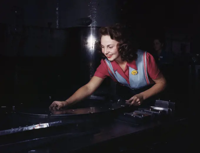 Metal parts are placed on masonite by this woman employee before they slide under the multi-ton hydropress, North American Aviation, Inc., Inglewood, Calif. - October 1942. 