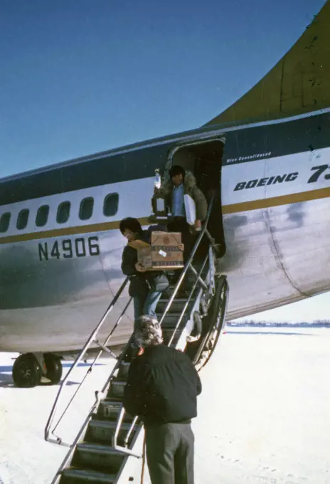 Carl Huntington and his wife exit a Wien Consolodiated airplane at Galena, Alaska, Carl is holding his trophy from winning the 1974 Iditarod Race ca. March 1974. 