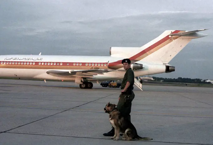 1980 - A security policeman and sentry dog watch as a Jordanian airliner departs with King and Queen Hussein Bin-Talal aboard.. 