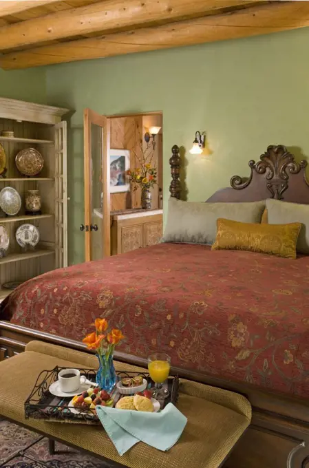 Breakfast tray with flowers at end of bed with floral cover and ornate mahogany head rest. 