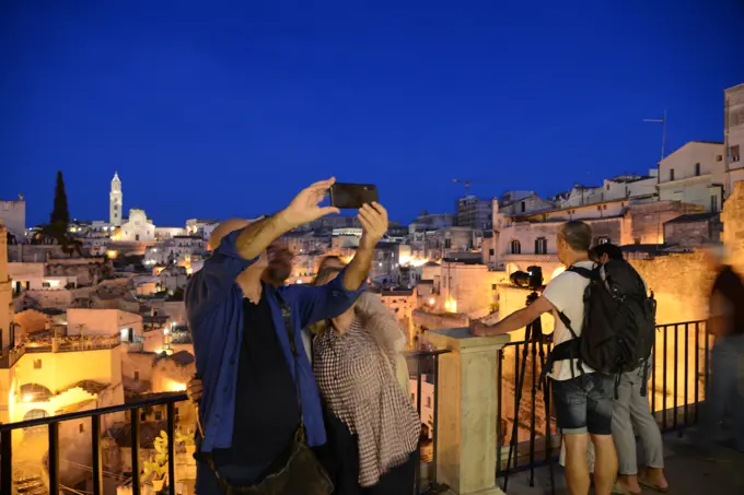 Tourist taking pictures and selfies. At night with suggestive lights the Pontifical Basilica Cathedral of Maria Santissima della Bruna and Sant'Eustachio dominates the view over Matera. Matera is a city located on a rocky outcrop. The so-called area of the Sassi (Stones) is a complex of cave houses carved into the rock, Basilicata, Italy, Europe