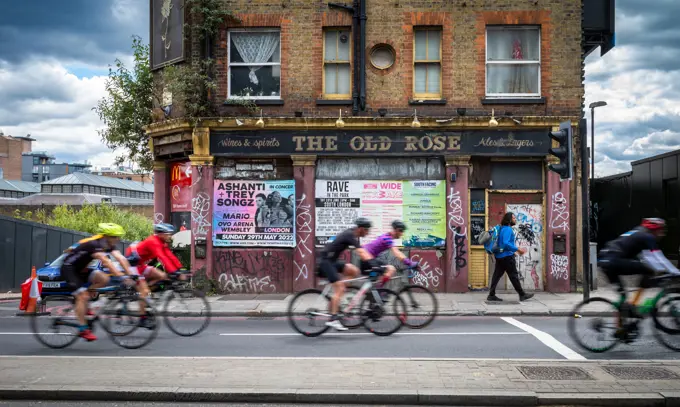 A group of cyclists participating in RideLondon 2022 pass a derelict pub called The Old Rose in the East End of London. The event was held for the first time since 2019 and the route took around 20,000 participants into Essex and across London.