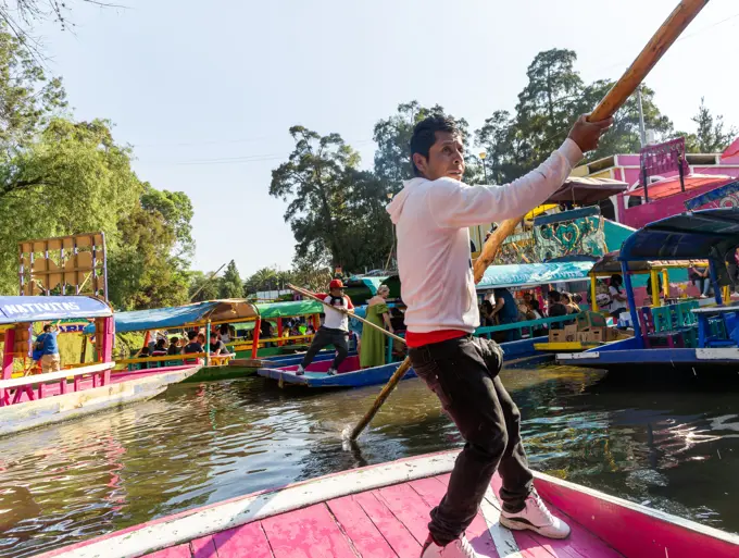 Popular tourist attraction people boating on colorful barges on canal at Xochimiloco, Mexico City, Mexico, trajinero punting barge.