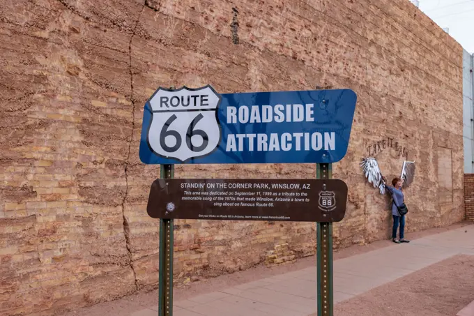 Woman posing for a photo behind roadside attraction sign at Standin' on the Corner Park in downtown Winslow, Arizona.