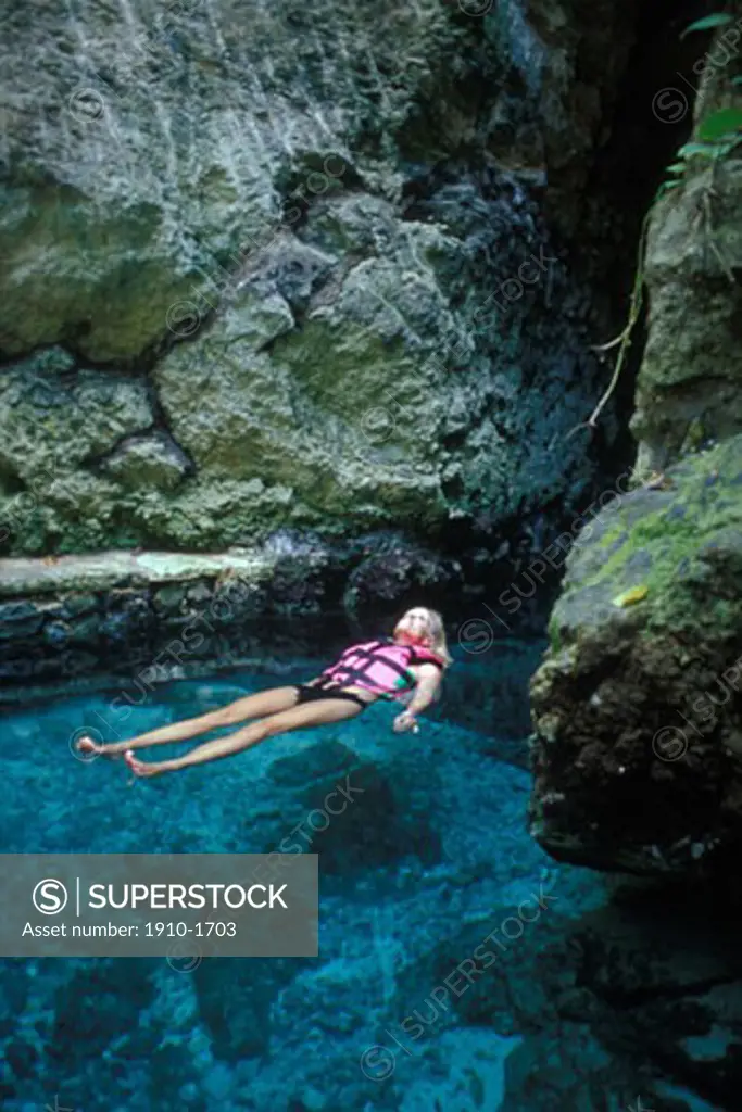 Woman floating along in natural river course leading to underground cavern Xcaret tourist park MEXICO Quintana Roo