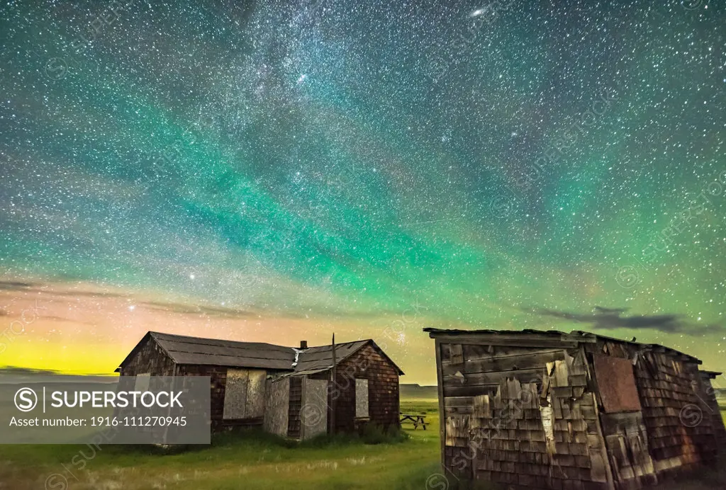 The Pleiades rising behind the rustic cabins and outbuildings of the historic Larson Ranch in Grasslands National Park, Saskatchewan. Aurora shines to the left in the north while green airglow illuminates the sky to the east above the buildings. Grasslands is a Dark Sky Preserve. And the sky is very dark. All illumination here is natural  note the dark clouds seen against the brighter airglow-lit sky. This is a stack of 4 exposures for the ground to smooth noise and one exposure for the sky, 