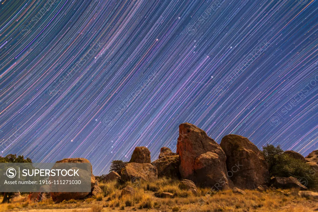 Star trails showing Orion and Taurus rising behind the rock formations of City of Rocks State Park, New Mexico. I shot this Monday, Dec 29, 2014. The colours of the stars and trails have been boosted in vibrancy to show the colour differences better. Red Betelgeuse is at left, while the pinkish Orion Nebula is at centre. The cyan trail at right is Comet Lovejoy (C/2014 Q2). Light from the waxing quarter Moon illuminates the foreground. A satellite streak is at right of centre.This is a stack o