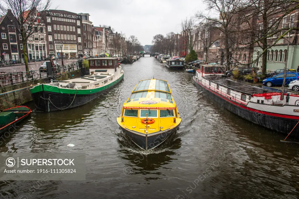 A bright yellow boat floats on the Amsterdam Canal in Amsterdam, Netherlands